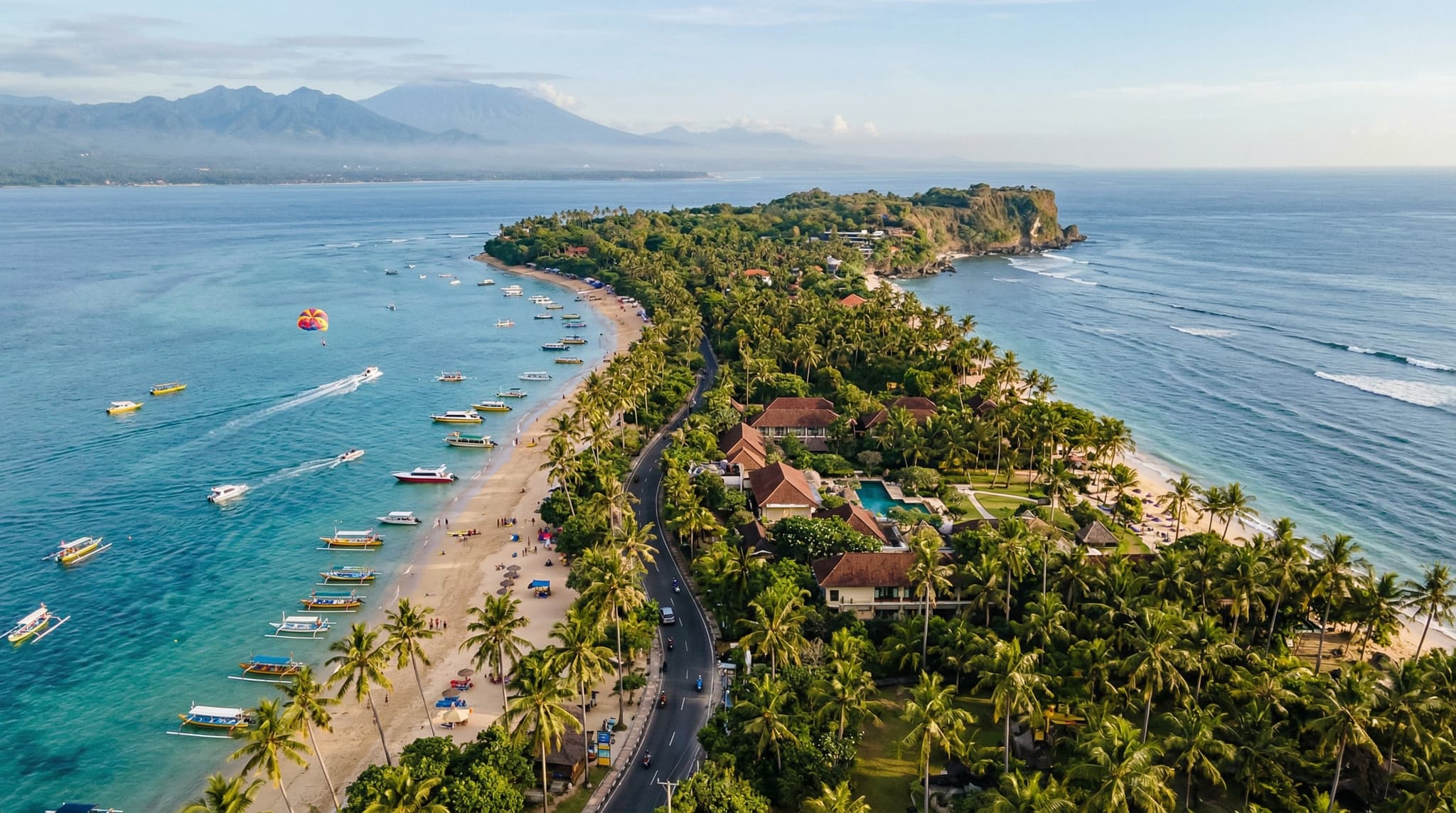 Aerial or wide coastal view of Tanjung Benoa's narrow peninsula with water sports activity visible on the calm bay — parasailing, boats, or jet skis on the water — establishing the article's central subject of Bali's water sports hub on the Nusa Dua peninsula