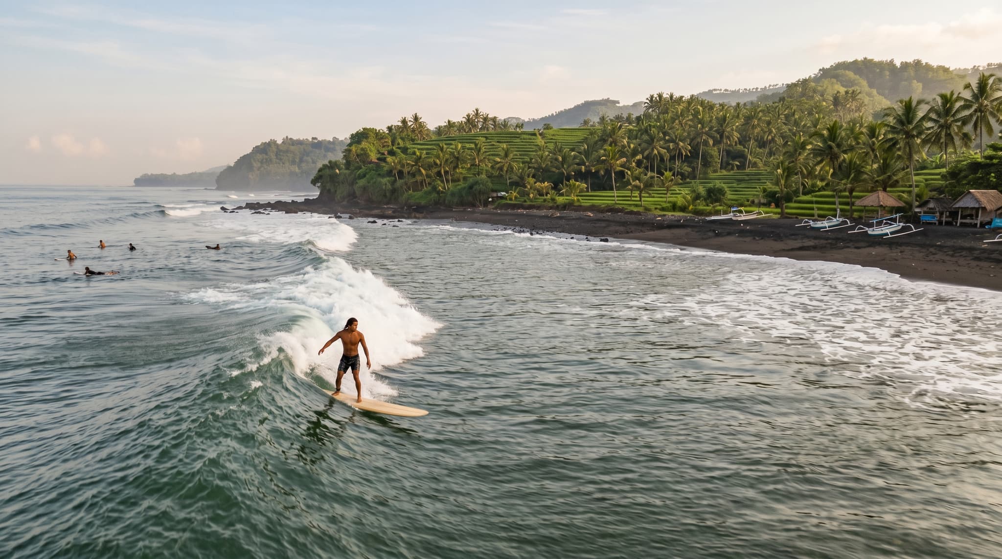 A longboarder riding a long, slow left-hand wave at Medewi Beach on Bali's black-sand west coast, with green terraced hills visible in the background — capturing the unhurried, uncrowded character of this remote surf break