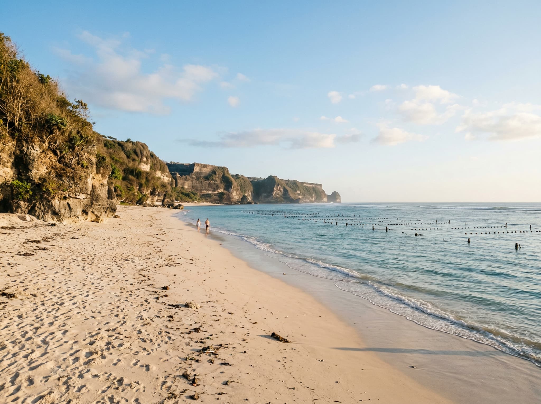 The quieter eastern stretch of Pandawa Beach away from the main parking area crowds — a walker or two on open sand with the limestone cliffs holding the skyline, illustrating the article's closing point that the beach rewards those who move past the obvious central section