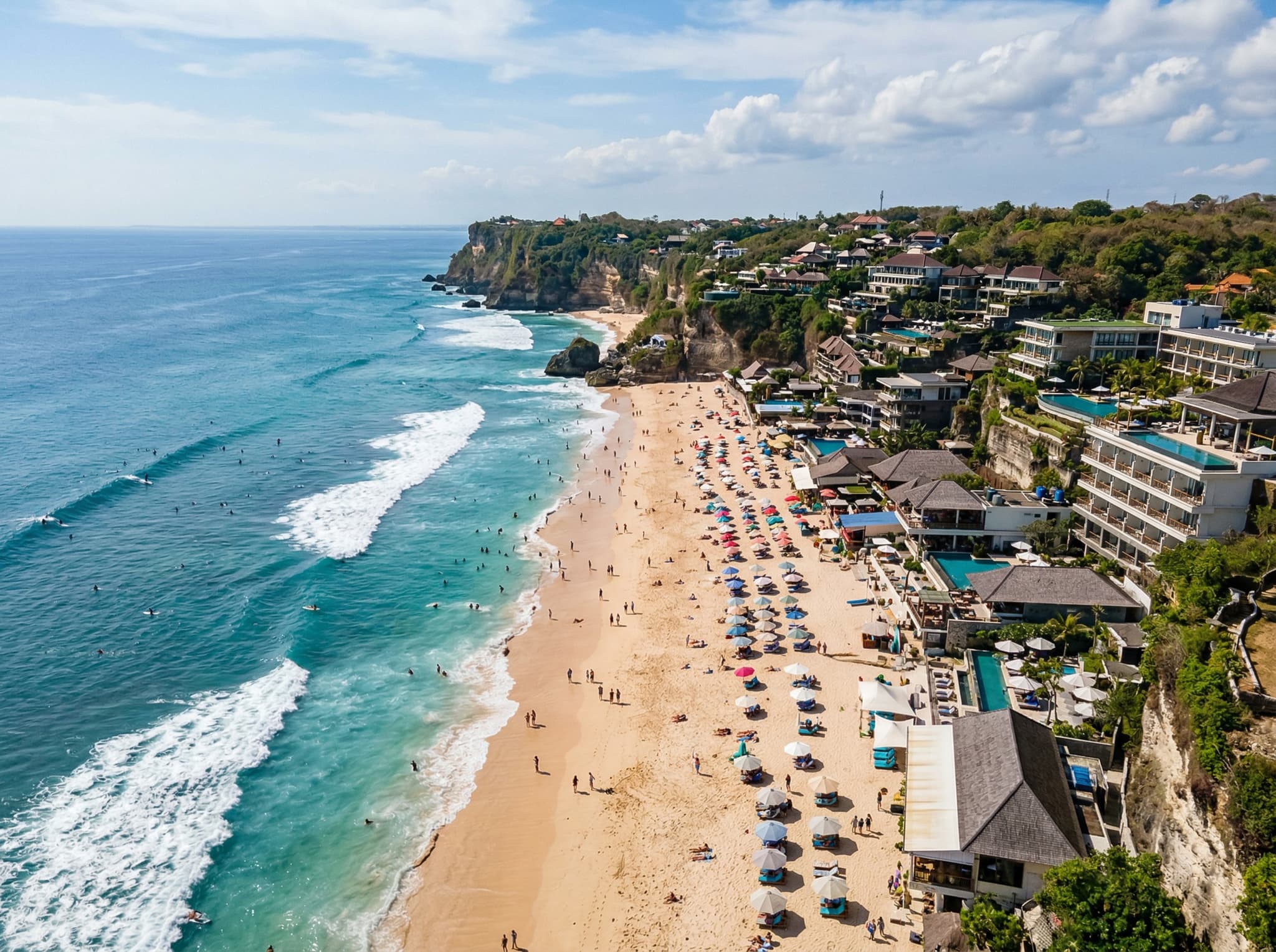 Dreamland Beach (Pantai Dreamland) on the Bukit Peninsula showing its wider sandy stretch and visible commercial development along the shore — illustrating the article's point that it has seen more development than neighboring beaches like Bingin.