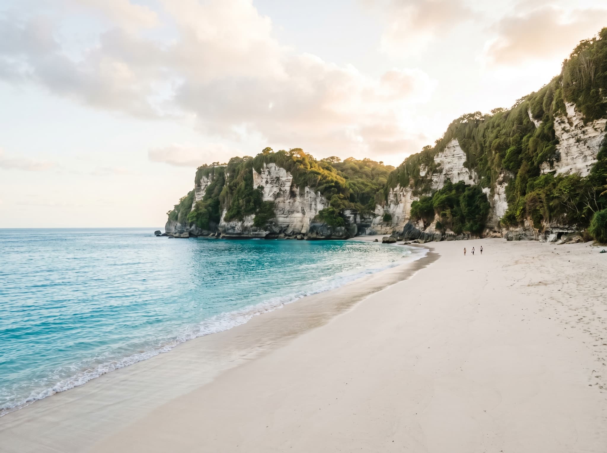 Gunung Payung Beach at sand level on a quiet weekday morning — clean white sand, turquoise water, and enclosing limestone cliff walls, with only a handful of visitors, conveying the solitude the article describes