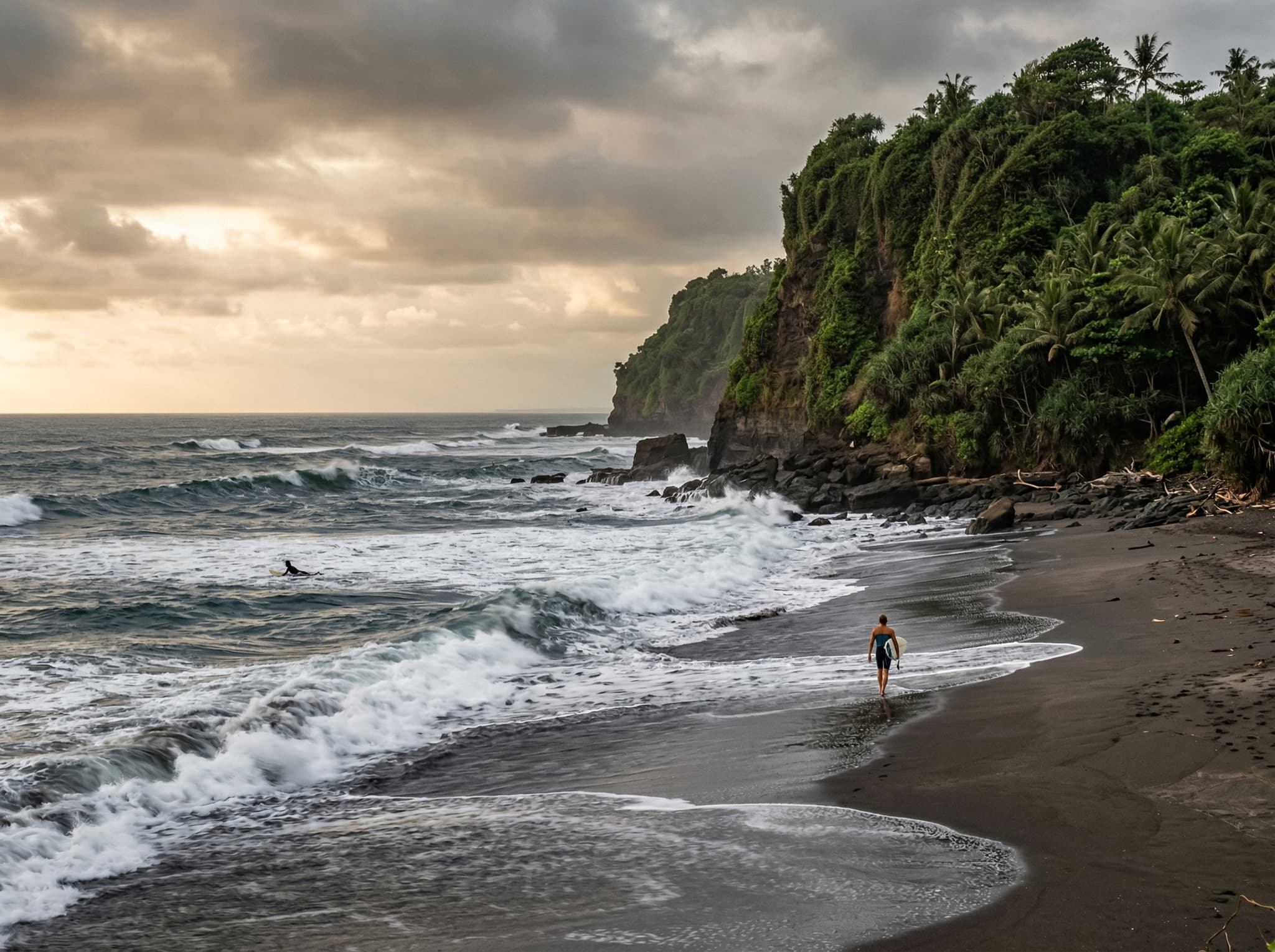 Kedungu Beach's dramatic dark sand shoreline backed by a cliff in Tabanan, Bali, with powerful surf breaking offshore — illustrating the raw, uncrowded beach that draws surfers and makes the Tipsy Pigs location worthwhile even for non-swimmers