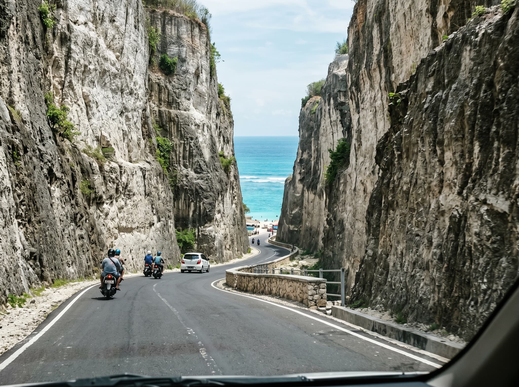 The dramatic paved road descending through a narrow gap in Melasti Beach's sheer limestone cliffs, with the first glimpse of turquoise water visible below — illustrating the article's point that the approach itself is half the experience and what makes Melasti unusual among Bukit beaches.