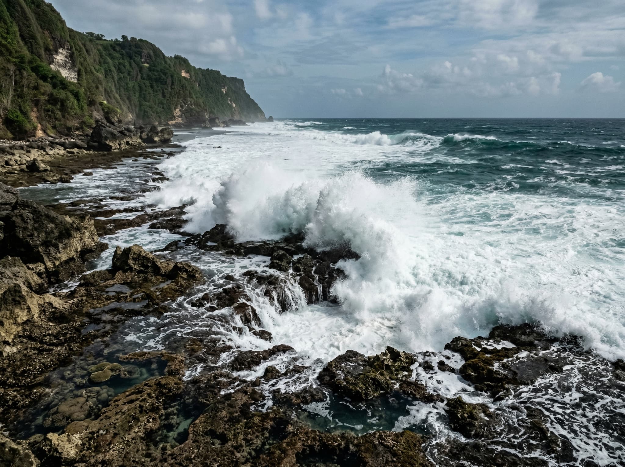 Waves breaking over shallow reef and exposed rocks at low tide on Nyang Nyang Beach, Bali — illustrating the strong currents and rocky conditions that make swimming dangerous for casual visitors, as warned in the article's swimming and surfing section