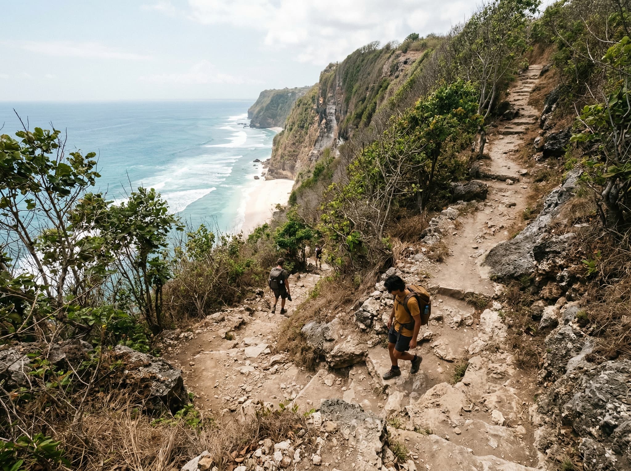 The steep cliff-top descent path leading down to Nyang Nyang Beach from the west entrance on Jalan Pantai Nyang-Nyang, Uluwatu — showing the rugged dirt trail and elevation drop that visitors must navigate to reach the beach, reinforcing the article's emphasis on earning the experience
