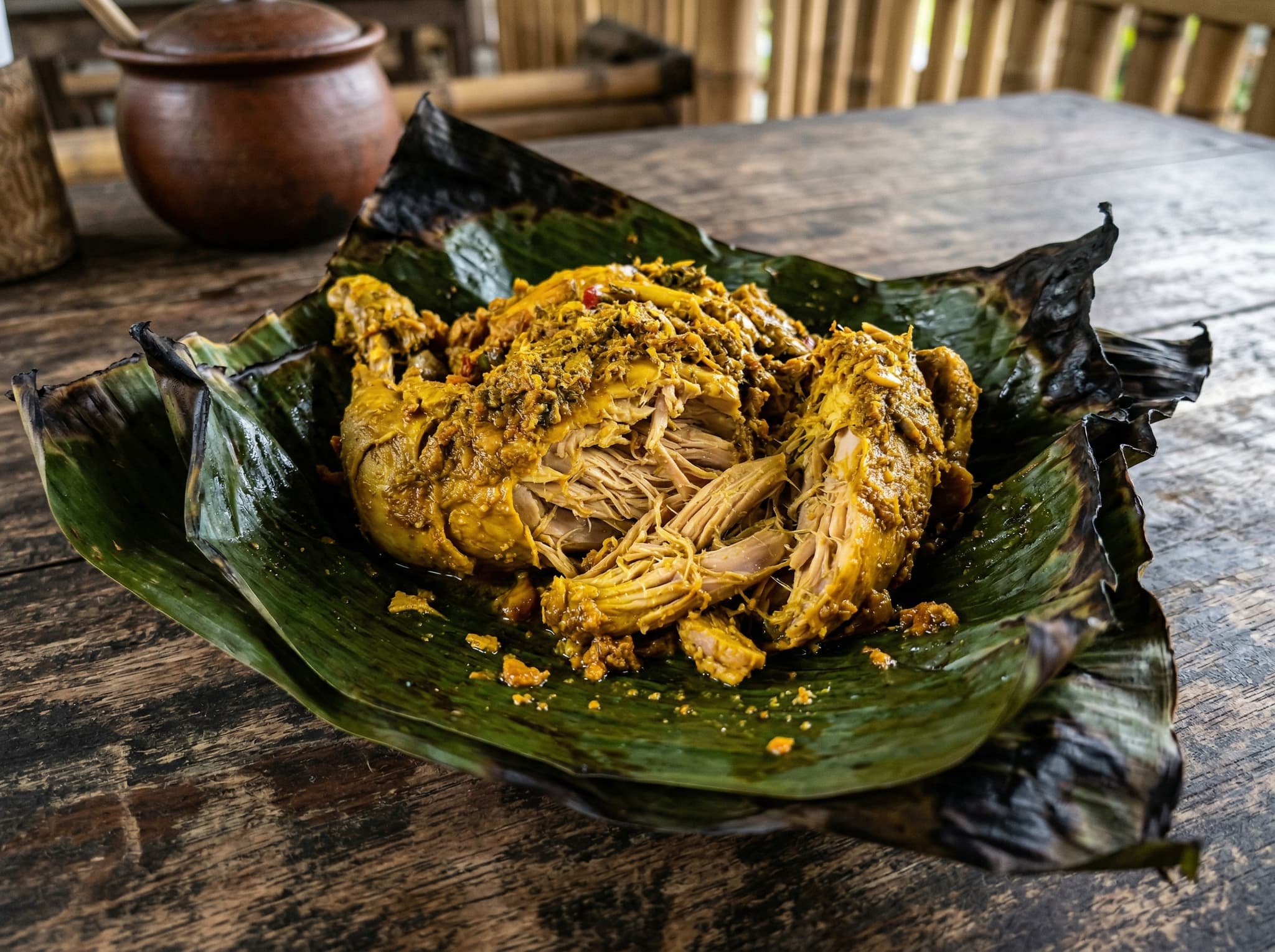 Close-up of ayam betutu — slow-cooked Balinese chicken wrapped in banana leaf — partially unwrapped to reveal turmeric-stained meat, the signature dish described in the What to Order section