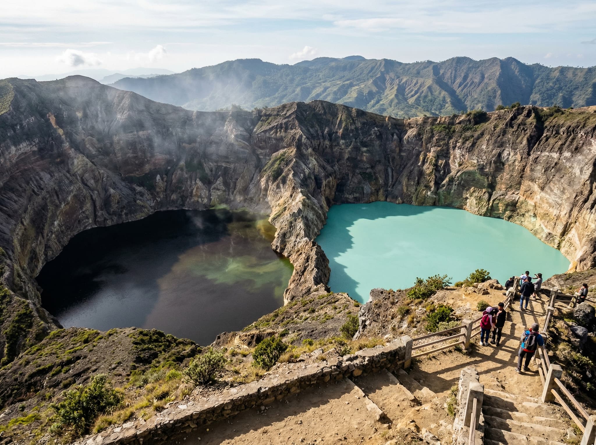 Close view of Kelimutu's adjacent crater lakes — Tiwu Ata Polo and Tiwu Koofai Nuwamuri — separated by a narrow volcanic ridge, showing the dramatic color contrast between the two bodies of water and the steep crater walls dropping to the water's edge