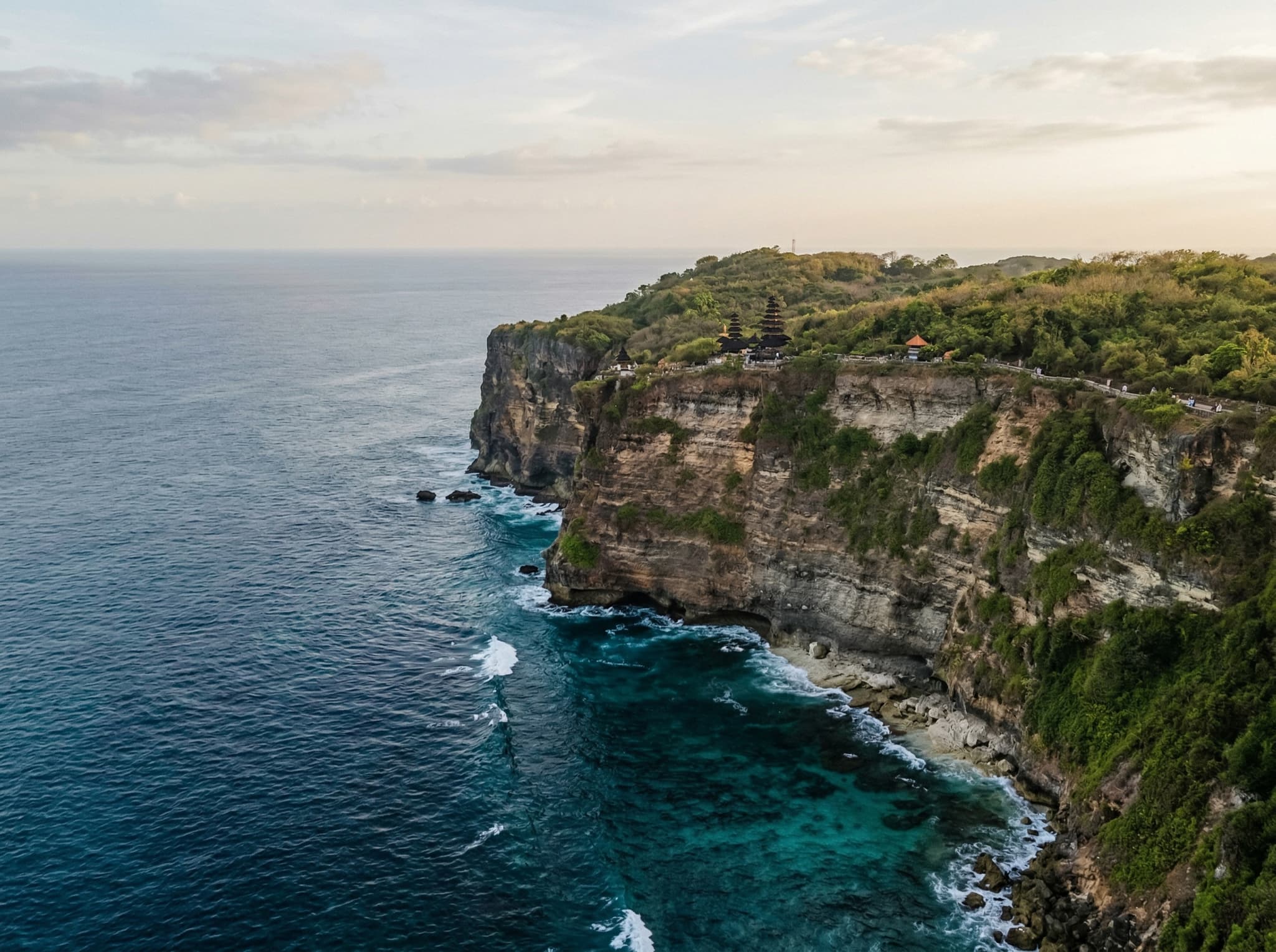 Uluwatu Temple cliffs in soft morning light with the Indian Ocean below, showing the dramatic limestone promontory from a distance — illustrating the article's tip about visiting in the morning for a quieter, crowd-free experience