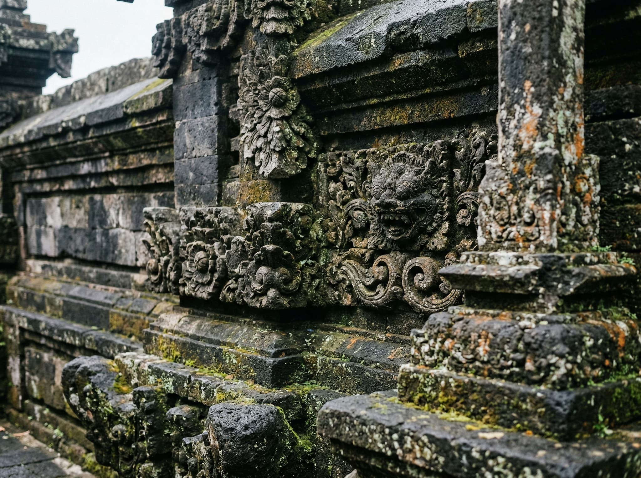 Close detail of Uluwatu Temple's moss-covered volcanic stone architecture — weathered dark stone with soft organic textures from centuries of salt wind — illustrating the article's description of the temple's modest, time-worn aesthetic and its spiritual significance