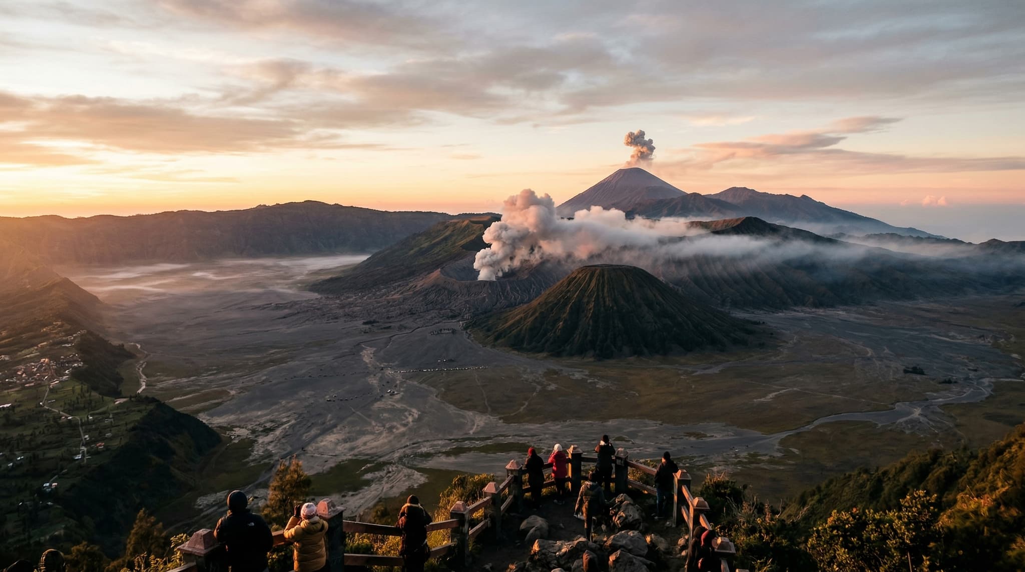 Mount Bromo's active volcanic crater venting sulfurous smoke at sunrise, with the vast grey Sand Sea of the Tengger caldera stretching below and Mount Semeru's cone rising in the background — the otherworldly landscape that draws travelers from Bali on a 10-hour journey across Java