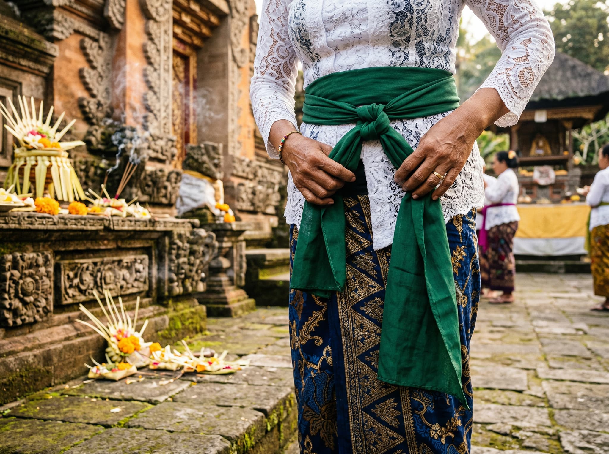 A visitor correctly tying or adjusting a sarong and sash at a Balinese temple, illustrating the practical wrapping instructions described in the final section of the article