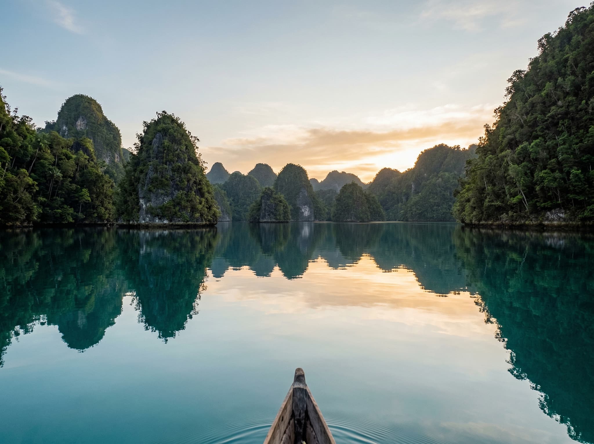 Kabui Bay at peak season — flat calm water, karst reflections, and the kind of empty, undisturbed scene the article promises even in high season, illustrating the closing line about looking up as much as down at the karst skyline reflected in glass-flat water