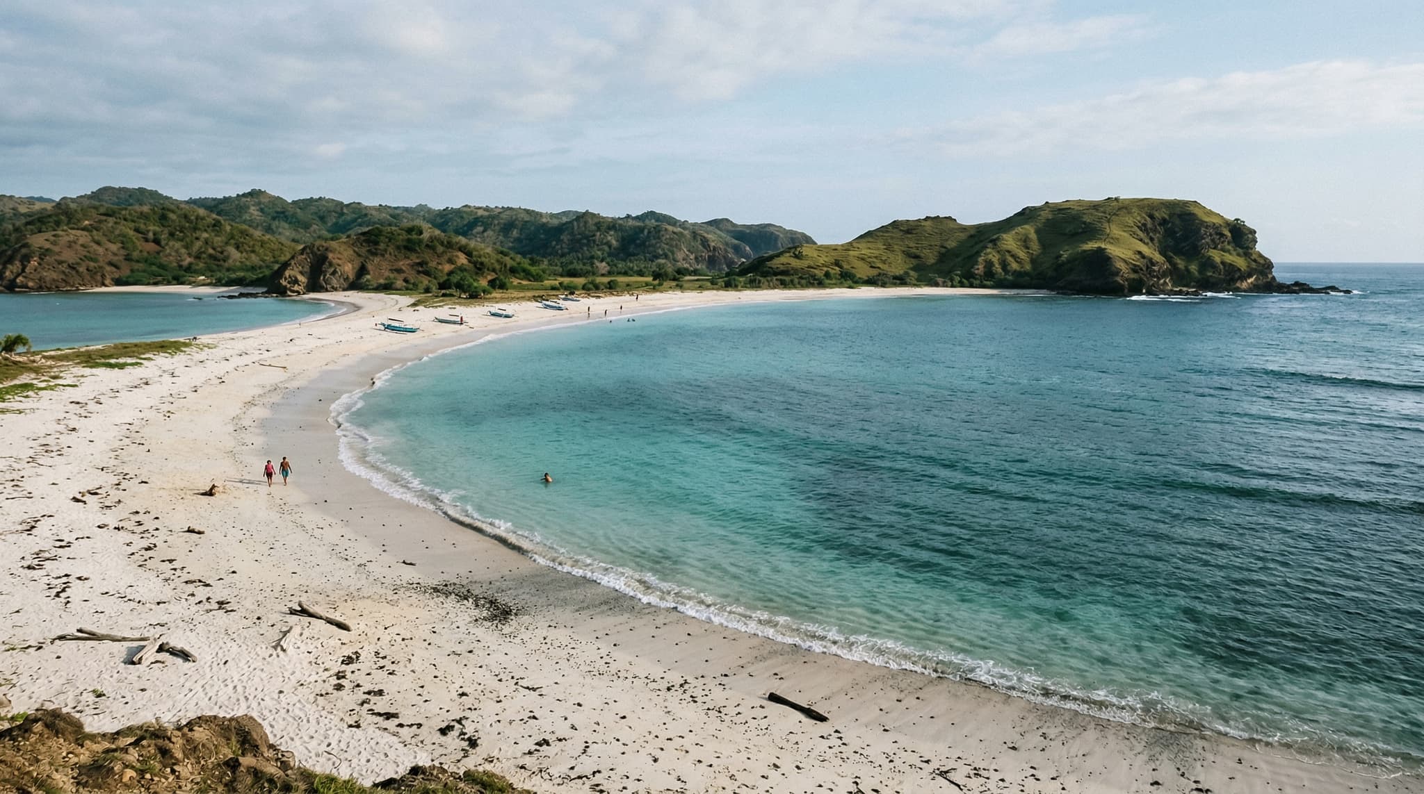 Tanjung Aan beach in South Lombok showing the distinctive white sand speckled with dark pepper grains, turquoise shallow water, and the twin-bay coastline — the defining image of a beach now caught between its natural beauty and incoming luxury development