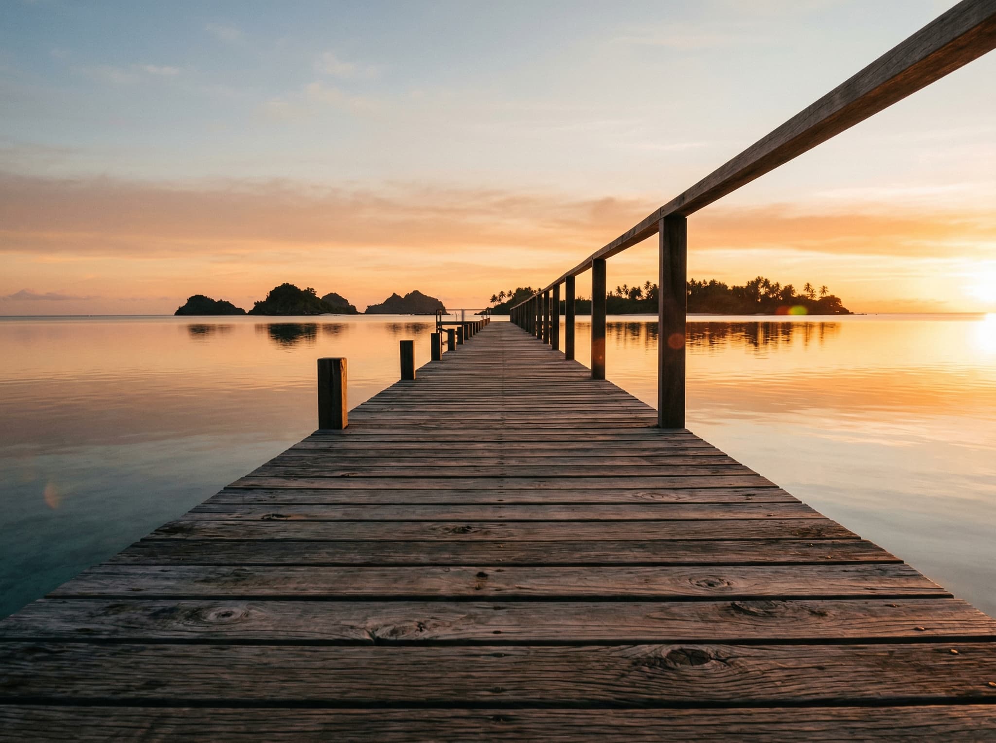 Golden hour or dusk view from Arborek's wooden jetty looking out over the Dampier Strait — evoking the quiet sunset the article reserves for overnight guests once day-trip liveaboards have departed, and the bioluminescent water that follows after dark
