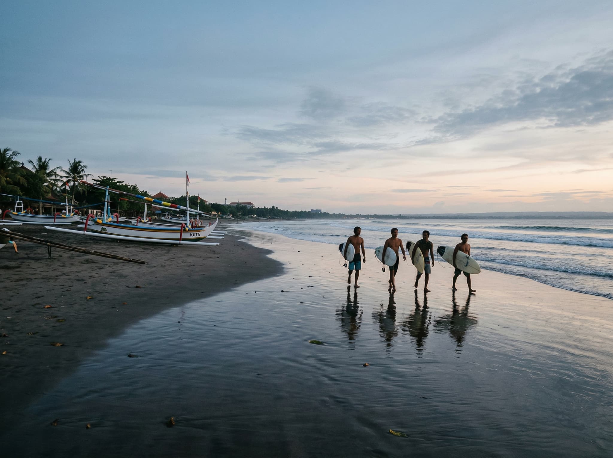 Early morning on Kuta Beach with local surfers and fishermen on the sand before the tourist crowds arrive, illustrating the quieter, more authentic side of the beach described in the article
