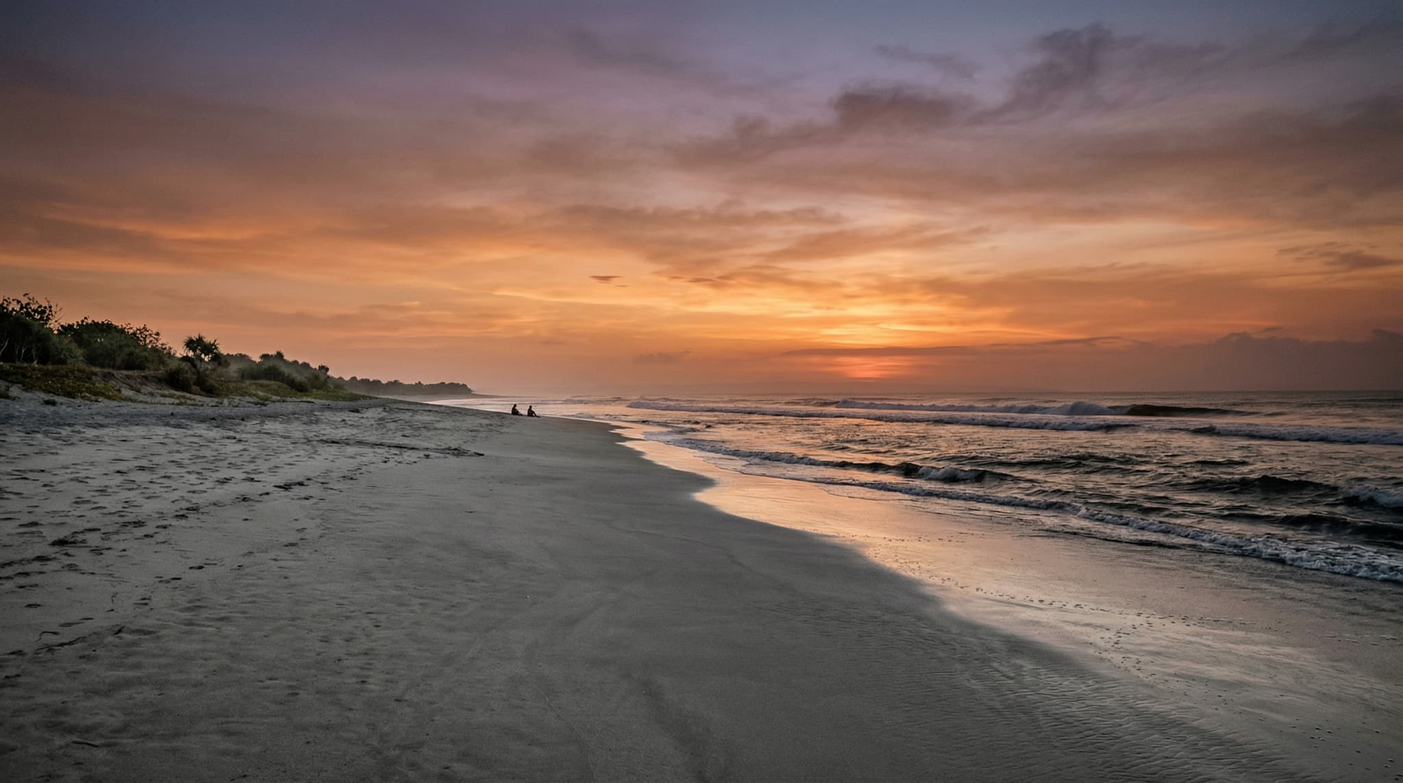 Pantai Batu Belig at late afternoon, showing the wide grey-white sand beach with the Indian Ocean surf and a warm copper sunset sky — illustrating the beach's unpolished, uncrowded character between Seminyak and Canggu