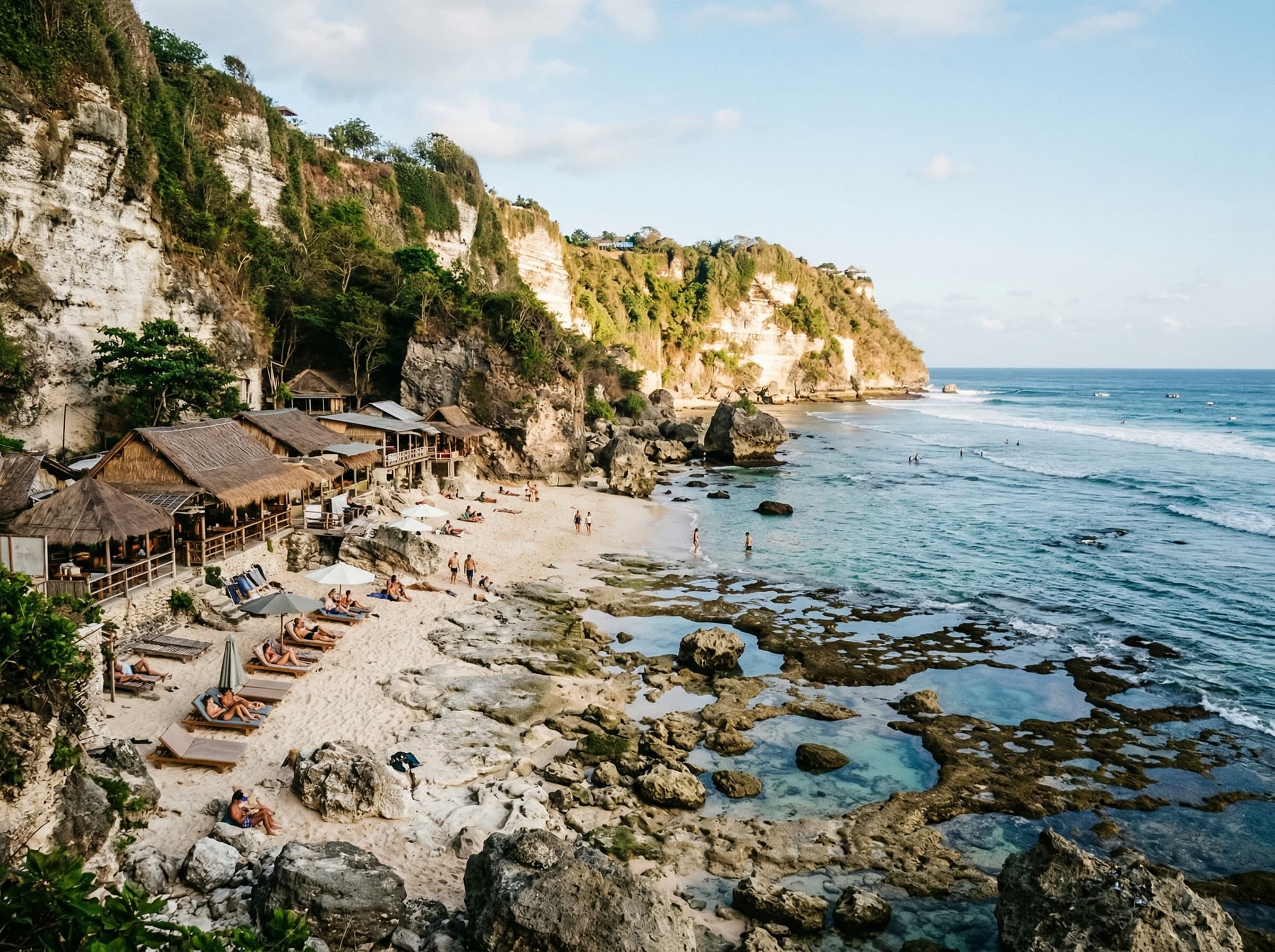 Bingin Beach at low tide showing the full width of the white sand, limestone boulders, and tide pools with the dramatic cliff backdrop — illustrating the intimate, pocket-sized scale of the beach described in the article