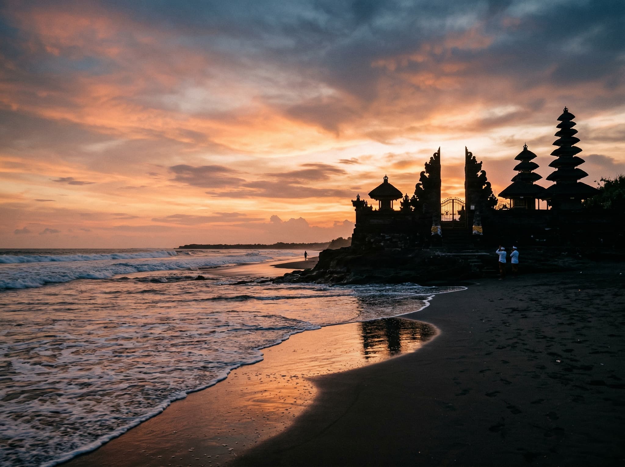Pura Masceti temple at Pererenan Beach, Bali at sunset — the dark stone temple gate silhouetted against a warm orange and pink sky, waves washing onto black sand in the foreground, no beach club infrastructure visible. Directly illustrates the article's callout tip about the temple sunset being one of the better free views on the coast.