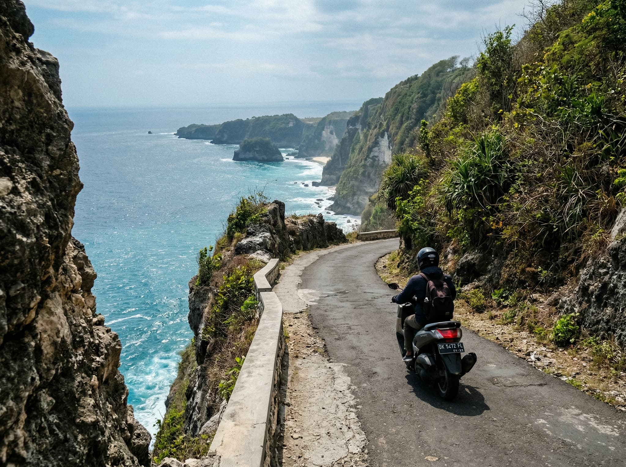 A scooter or motorbike on the narrow paved cliff road approaching Atuh Beach on Nusa Penida's eastern coast — illustrating the article's description of the route as fully paved but narrow, steep, and demanding confidence on the curves near the cliff edge